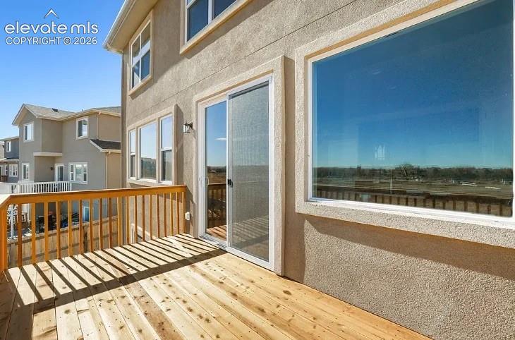 Elevated exterior deck featuring natural wood decking, a wooden railing, sliding glass doors, and stucco siding