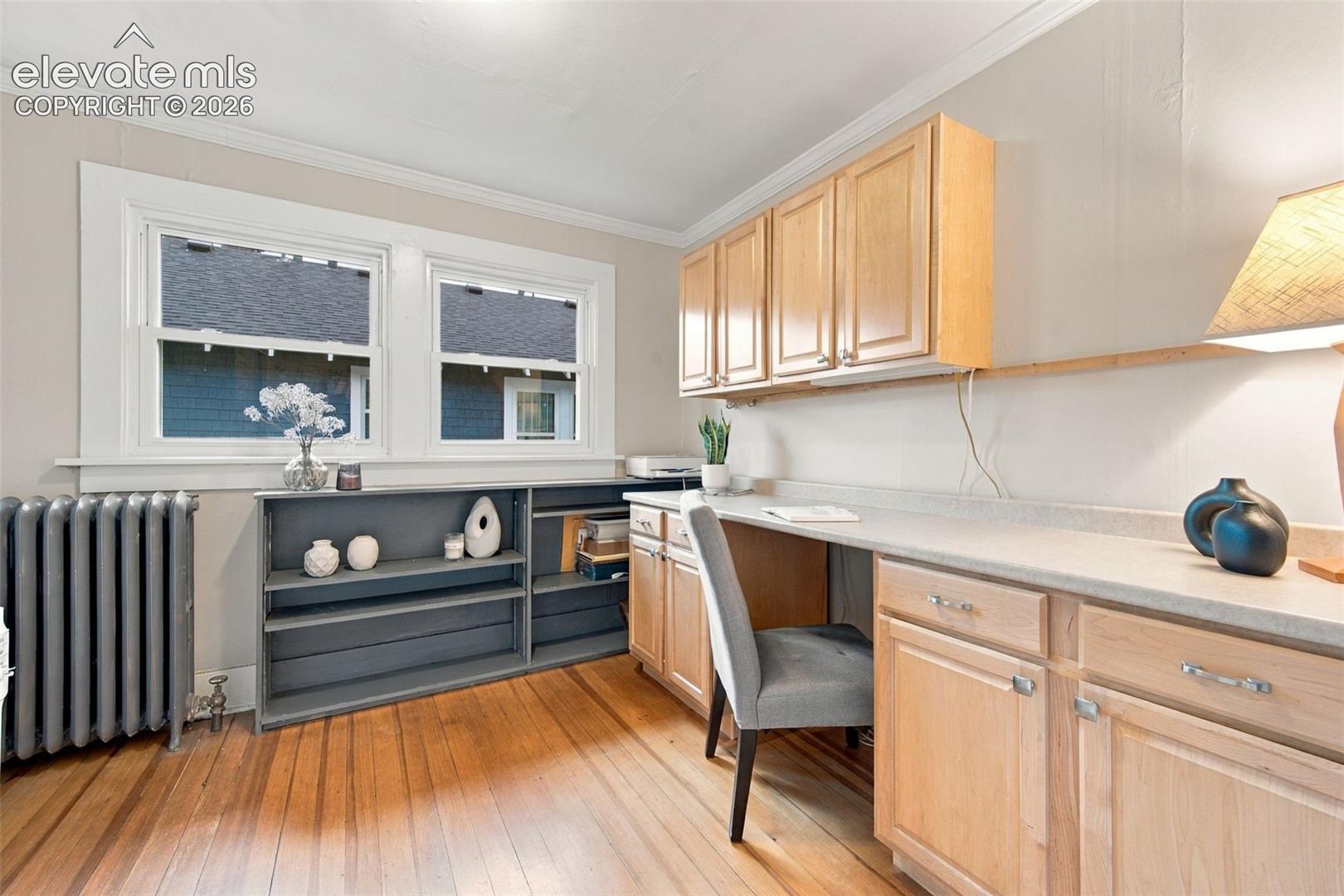 Hardwood flooring, natural wood cabinetry, solid surface countertop, built-in shelving, and cast iron radiator