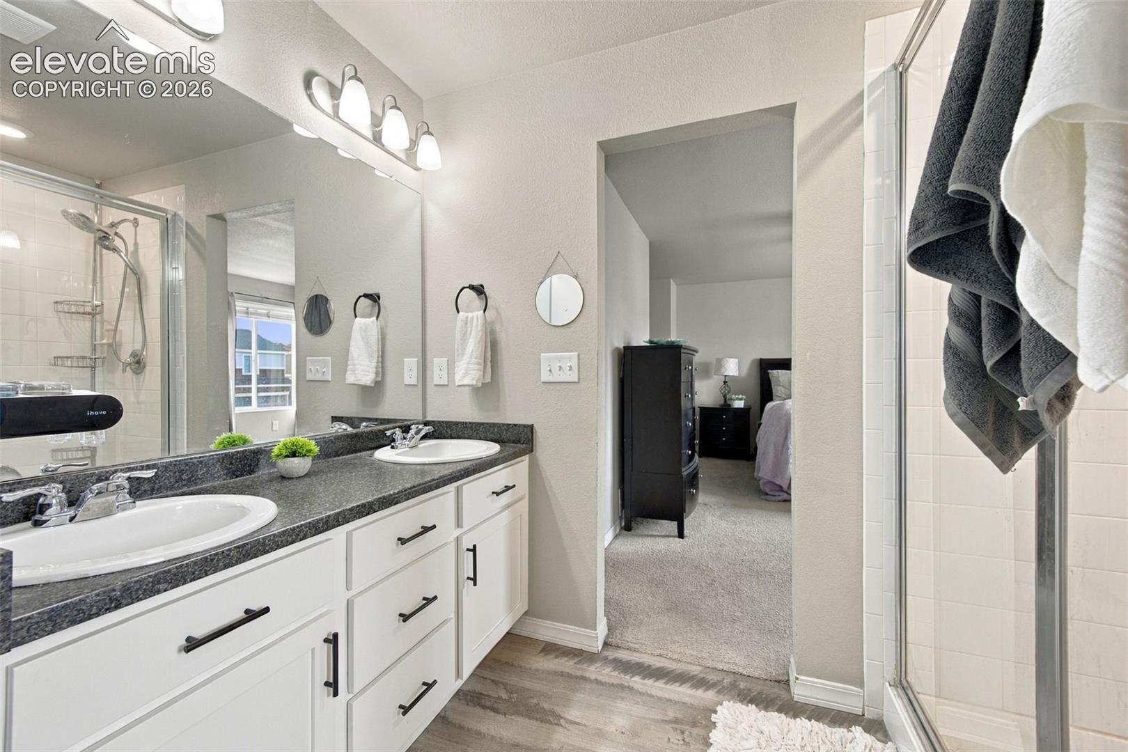 Double vanity featuring white cabinetry, dark stone-finish countertops, dual integrated sinks, and matte black hardware