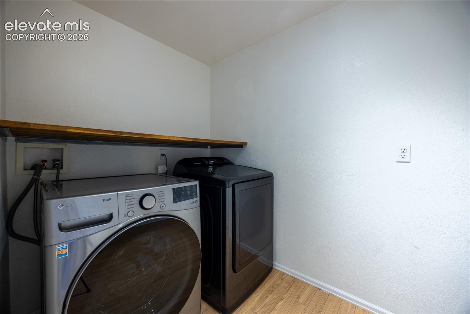 Compact laundry area with wood-finish flooring and a built-in wood shelf