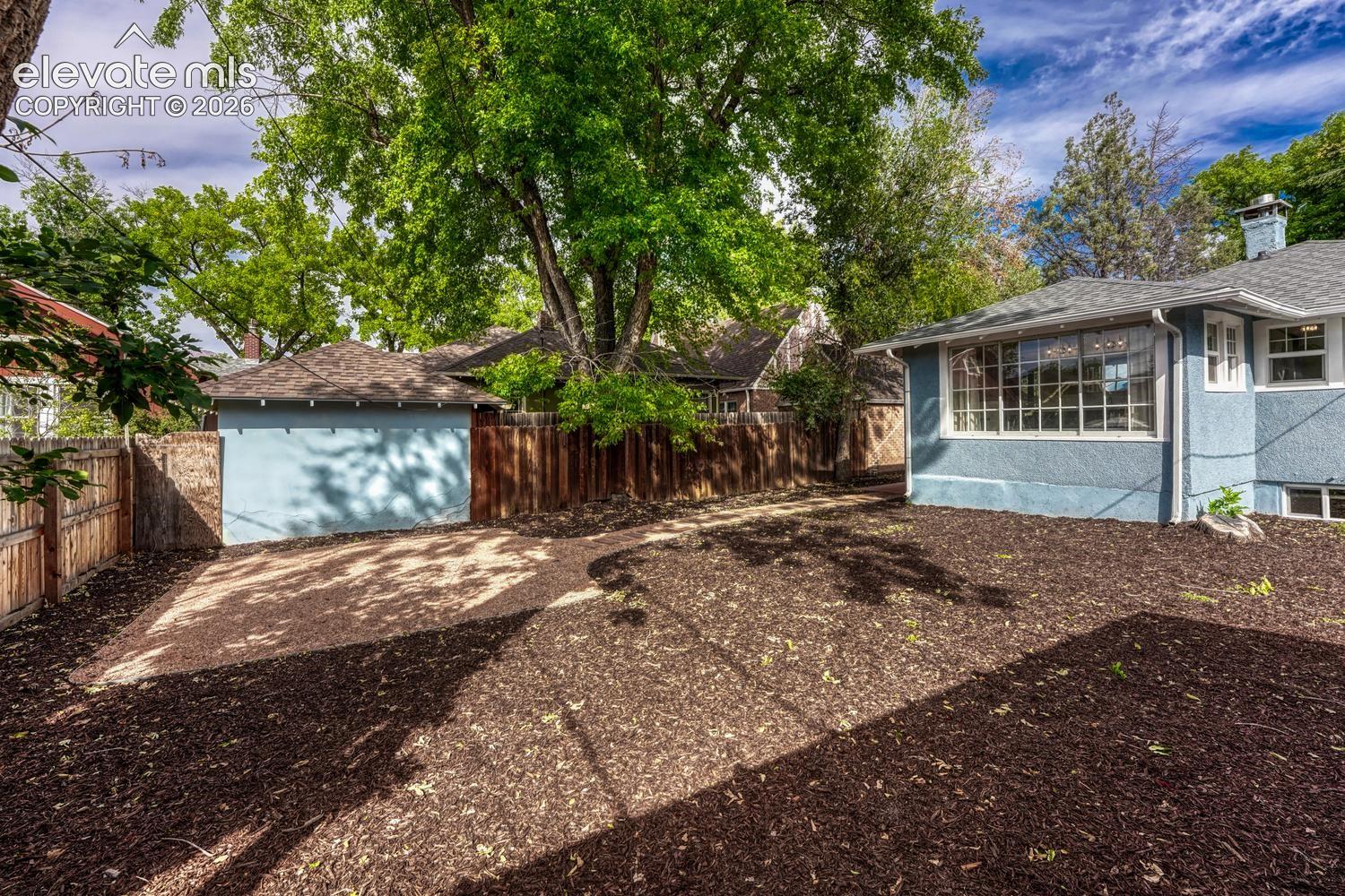 Private backyard featuring wood chip landscaping, a detached structure with a pitched roof, and a wood fence