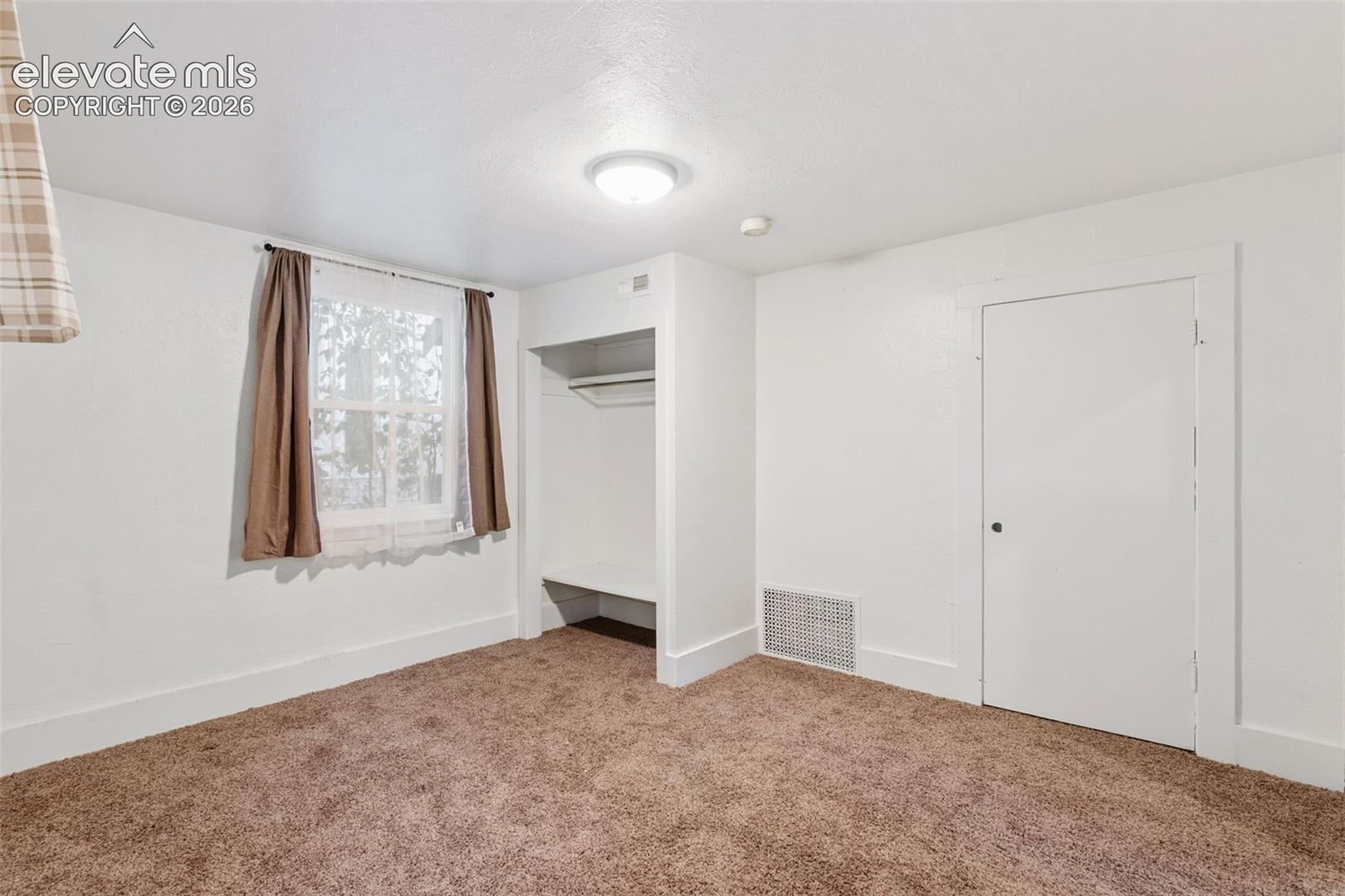 Neutral-toned carpeting, recessed closet with built-in shelving, single-hung window with casing, and solid-core interior door
