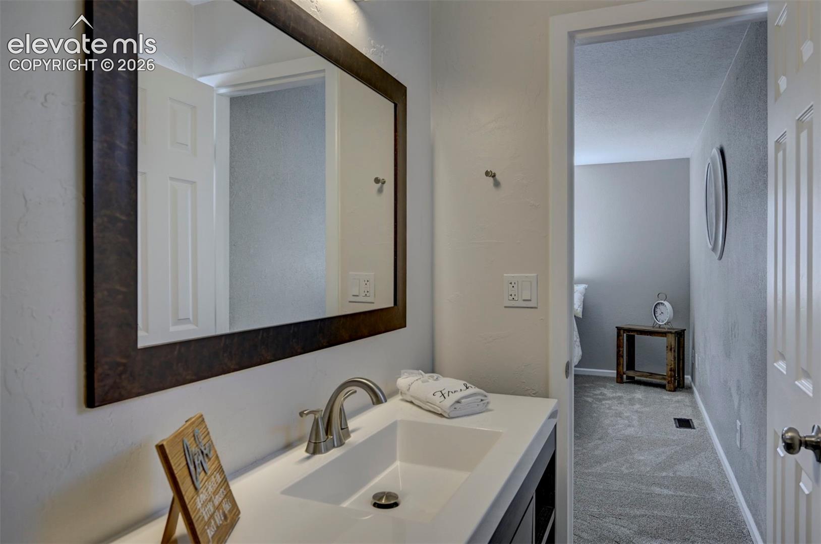 Vanity featuring a white countertop with an integrated rectangular basin, brushed-nickel widespread faucet, and large rectangular wall mirror with a dark wood-finish frame