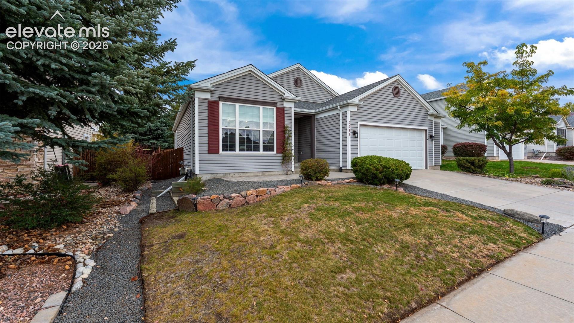 Single-story residence featuring horizontal siding, contrasting shutters, stone retaining wall, concrete driveway, and a two-car garage