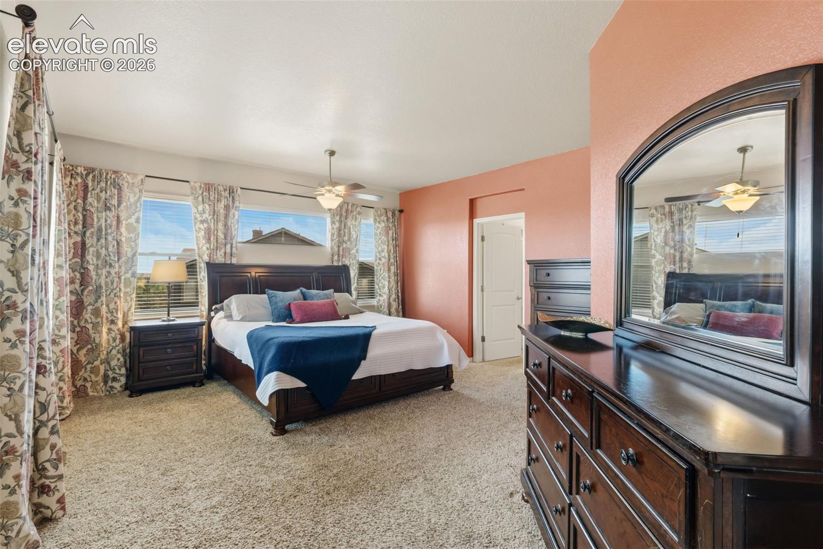 Carpeted bedroom featuring a ceiling fan, multiple windows with blinds, and a built-in dresser