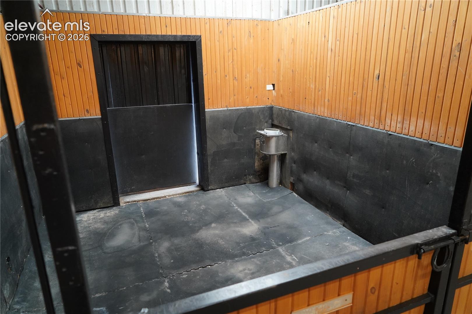 Wood-paneled stall with black-painted lower walls, a built-in water fixture, and rubber flooring