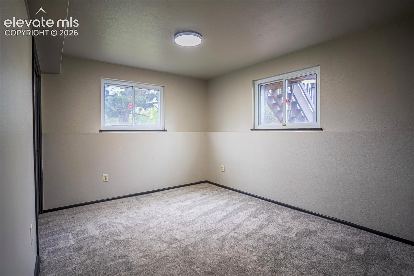 Neutral interior space featuring wall-to-wall carpeting, two sliding windows, and a flush-mount overhead light fixture