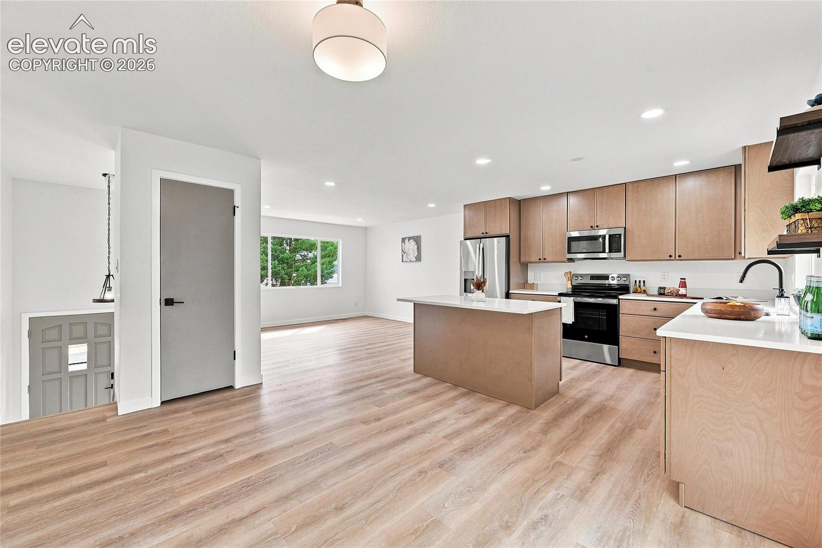 Open-concept layout featuring wood-finish flooring, a kitchen island with a white countertop, and stainless steel appliances