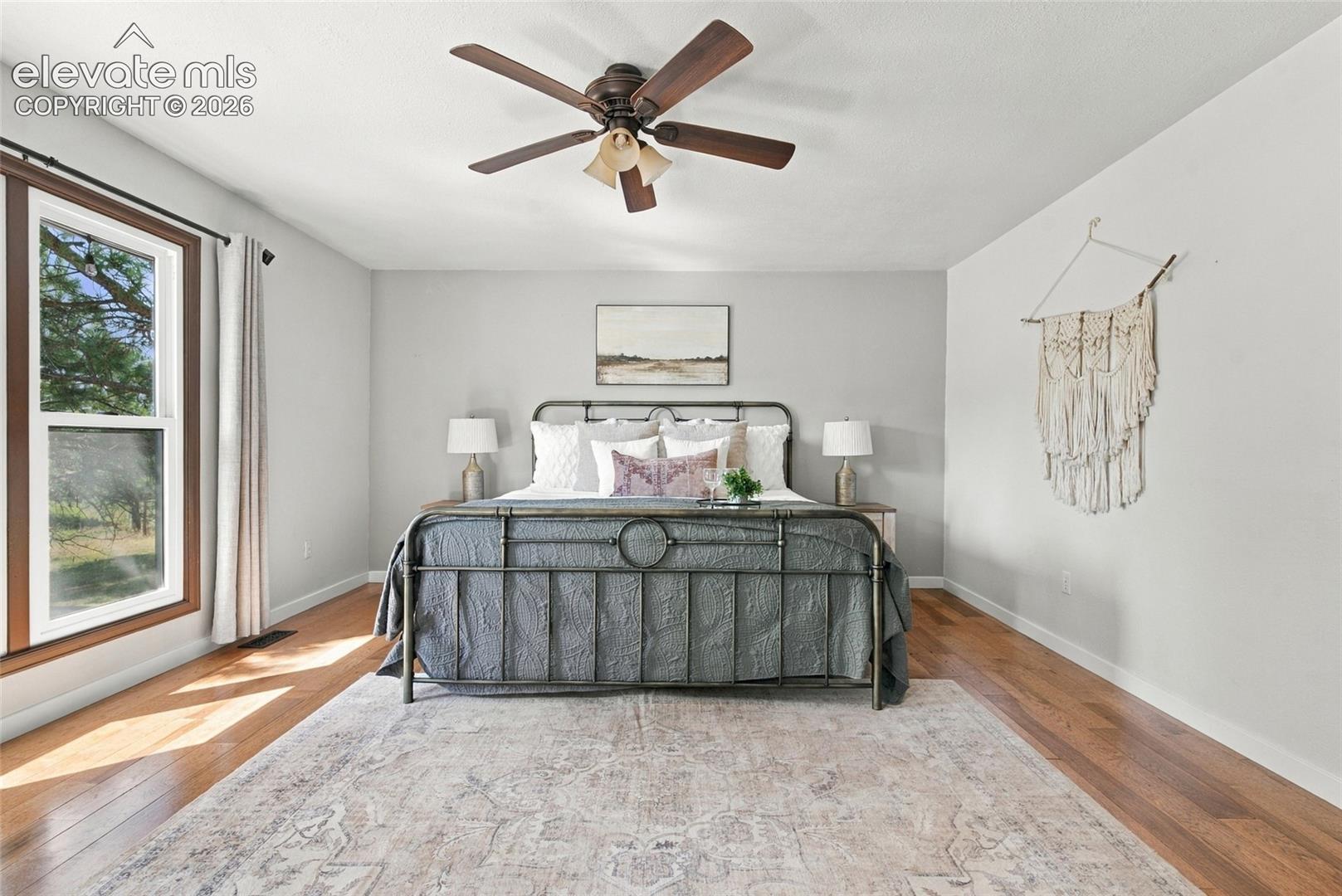 Hardwood flooring, a large window with wood trim, neutral wall tones, and a ceiling fan with integrated lighting