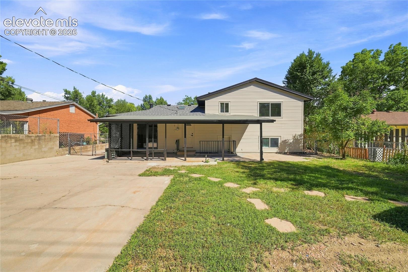 Expansive concrete patio with a covered outdoor area, complemented by a grassy yard and mature trees