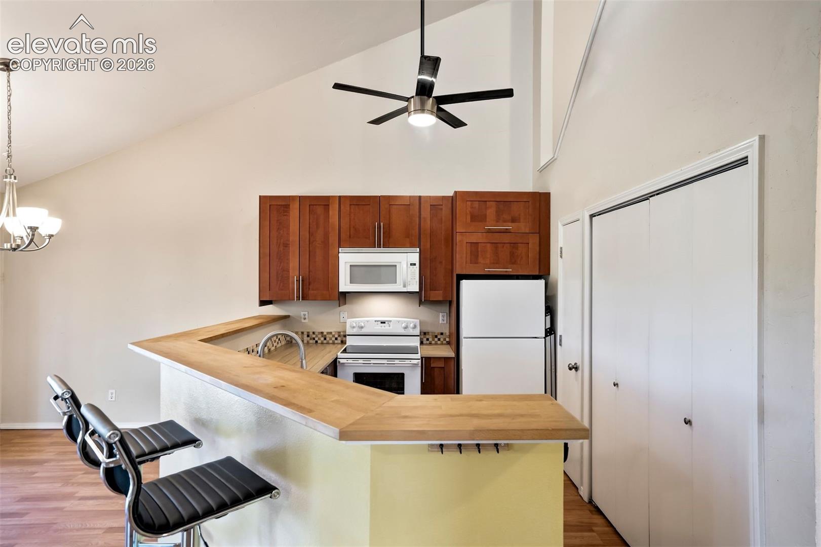 Vaulted ceilings featuring a modern ceiling fan, wood-finish cabinetry, wooden breakfast bar, and bi-fold closet doors