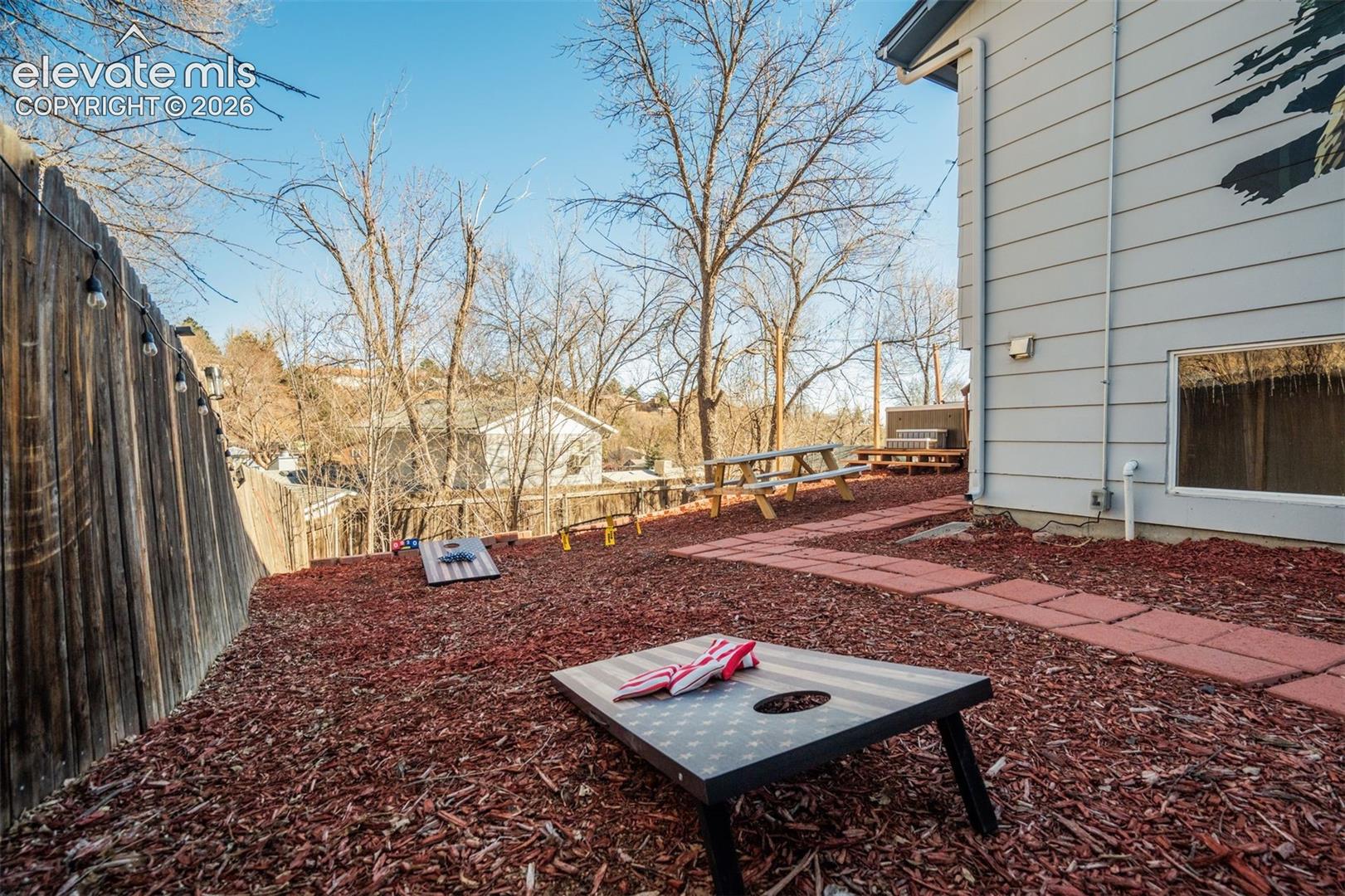 Expansive outdoor area featuring a wood fence, string lighting, and a terraced landscape with red mulch and stepping stones