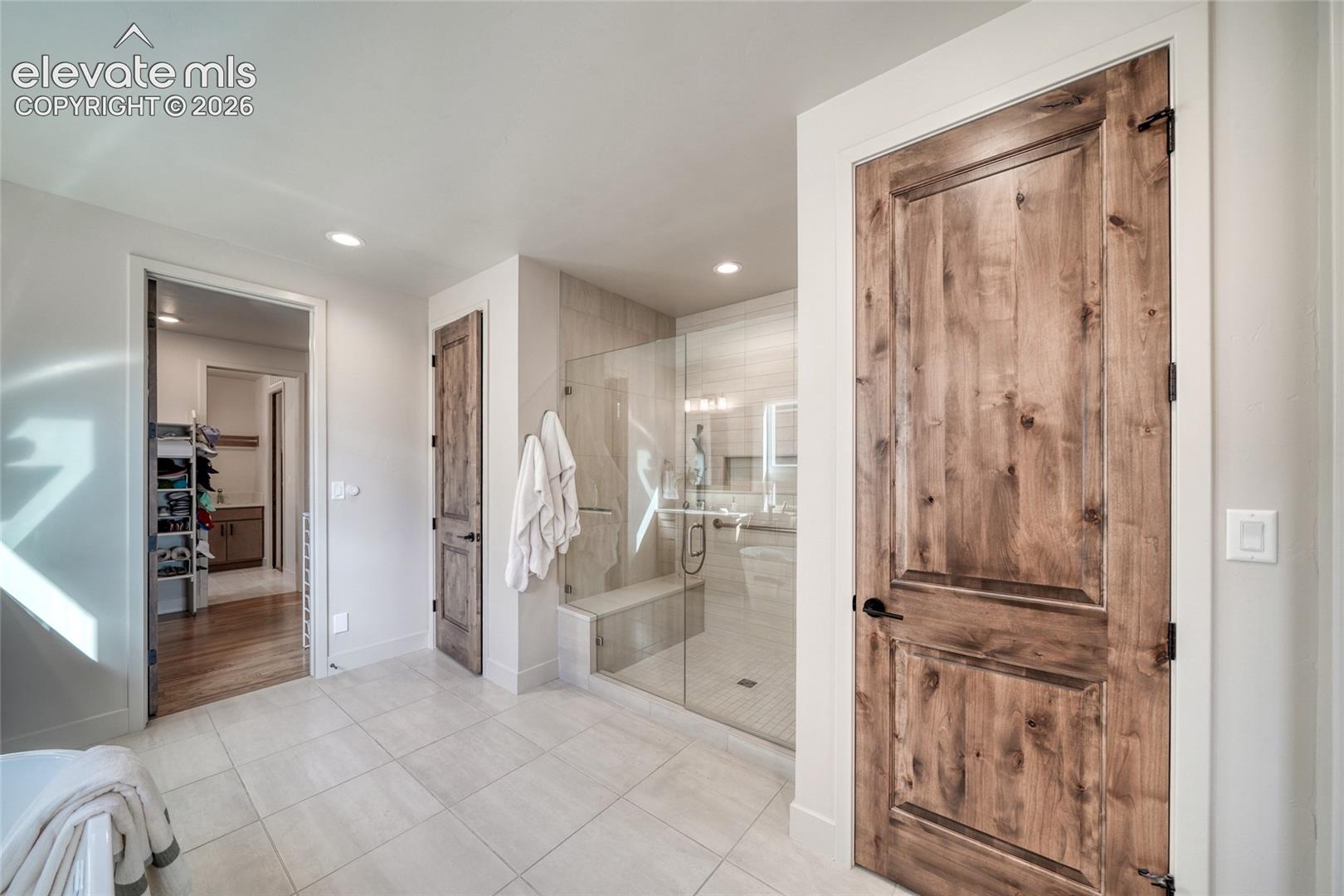 Glass-enclosed walk-in shower with stone tile surround and built-in bench, complemented by rustic-finish wood doors and large-format porcelain tile flooring