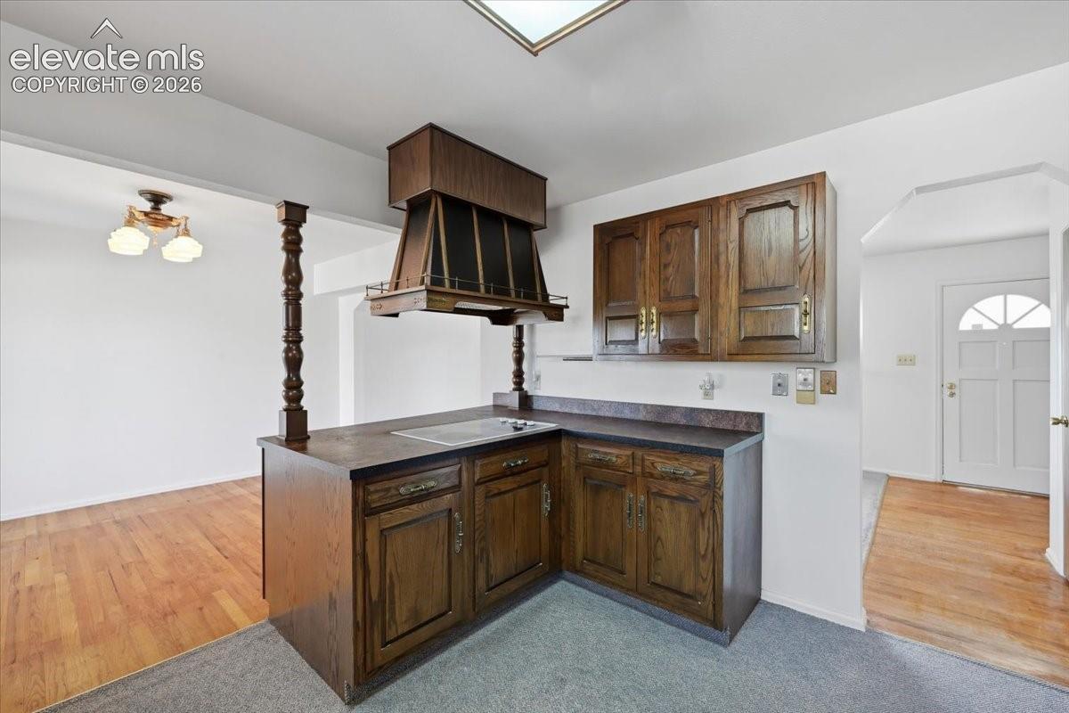 Kitchen featuring wood cabinetry, integrated range hood, solid-surface countertops, built-in cooktop, and wooden support post