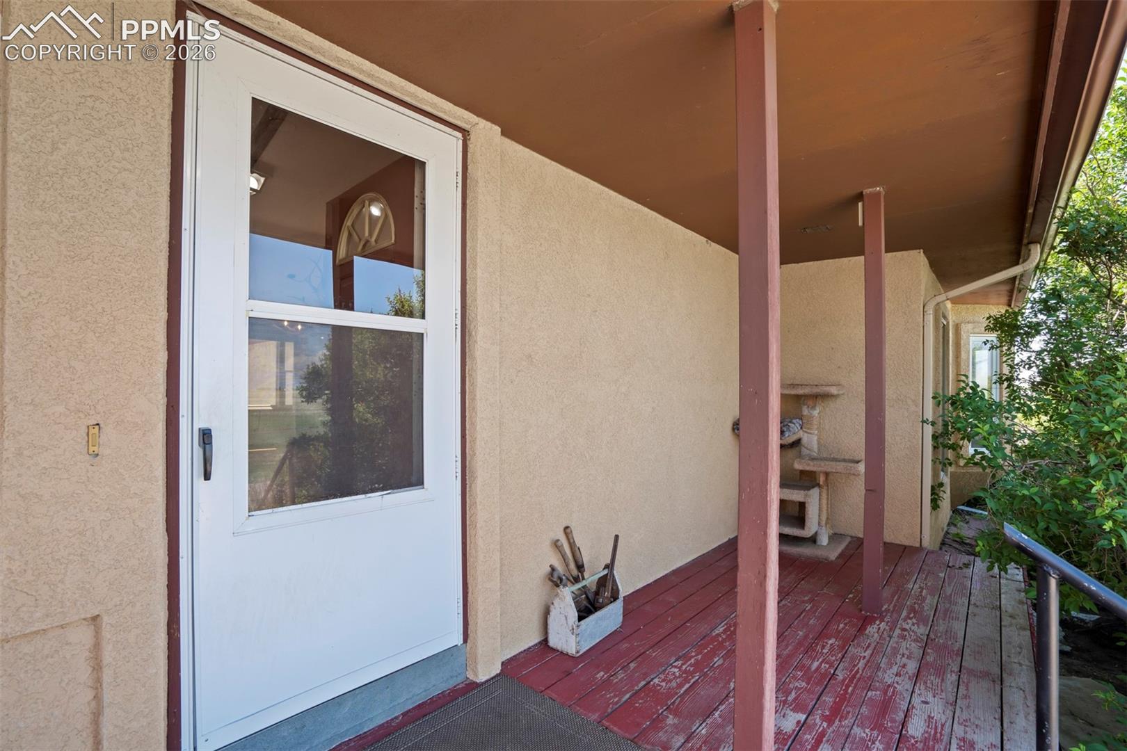 Covered front porch featuring a full-view storm door, textured stucco exterior, exposed wood support columns, and a wood-finish deck