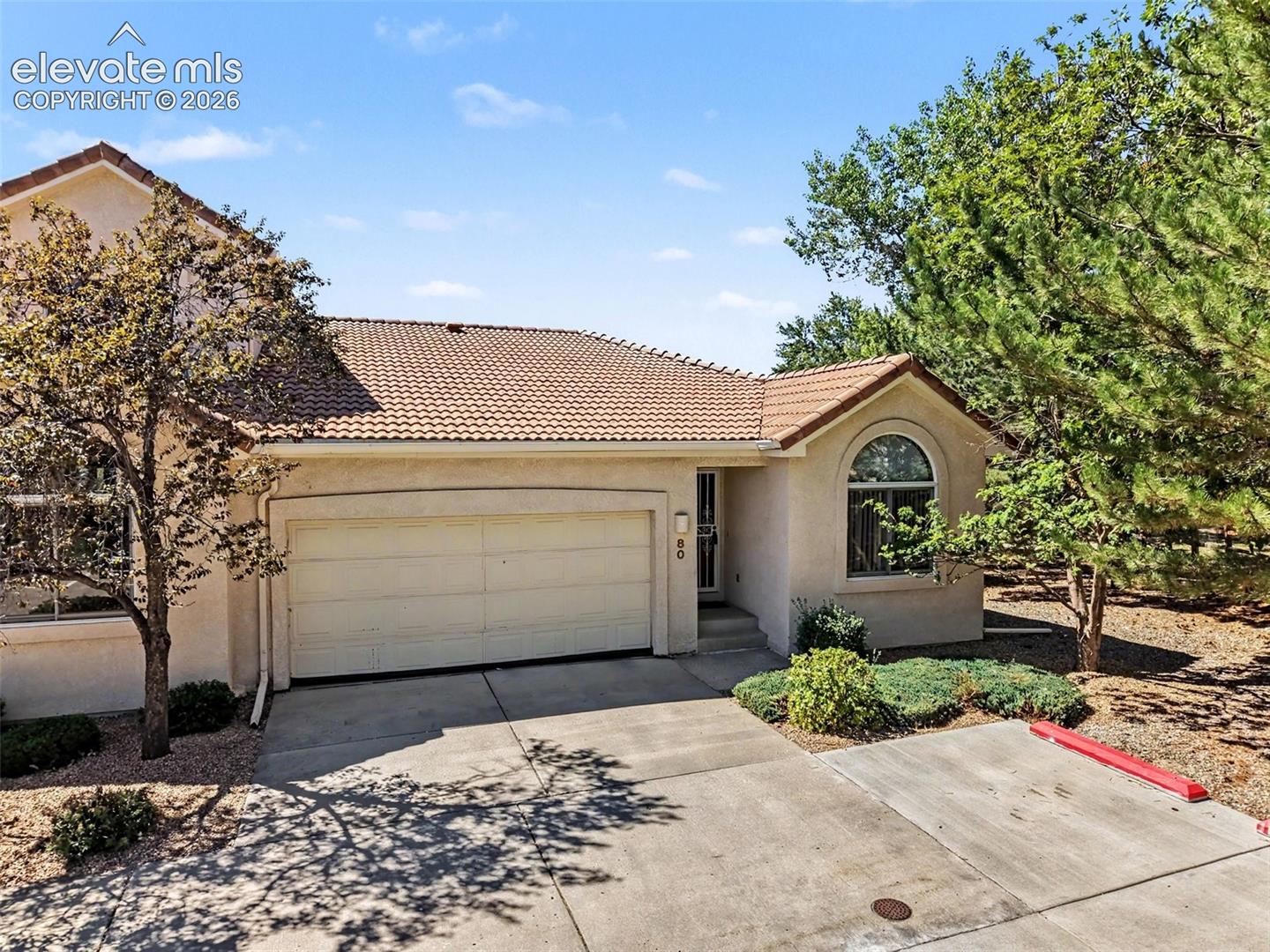 Stucco exterior featuring a tile roof, an arched window, and an attached garage with a concrete driveway