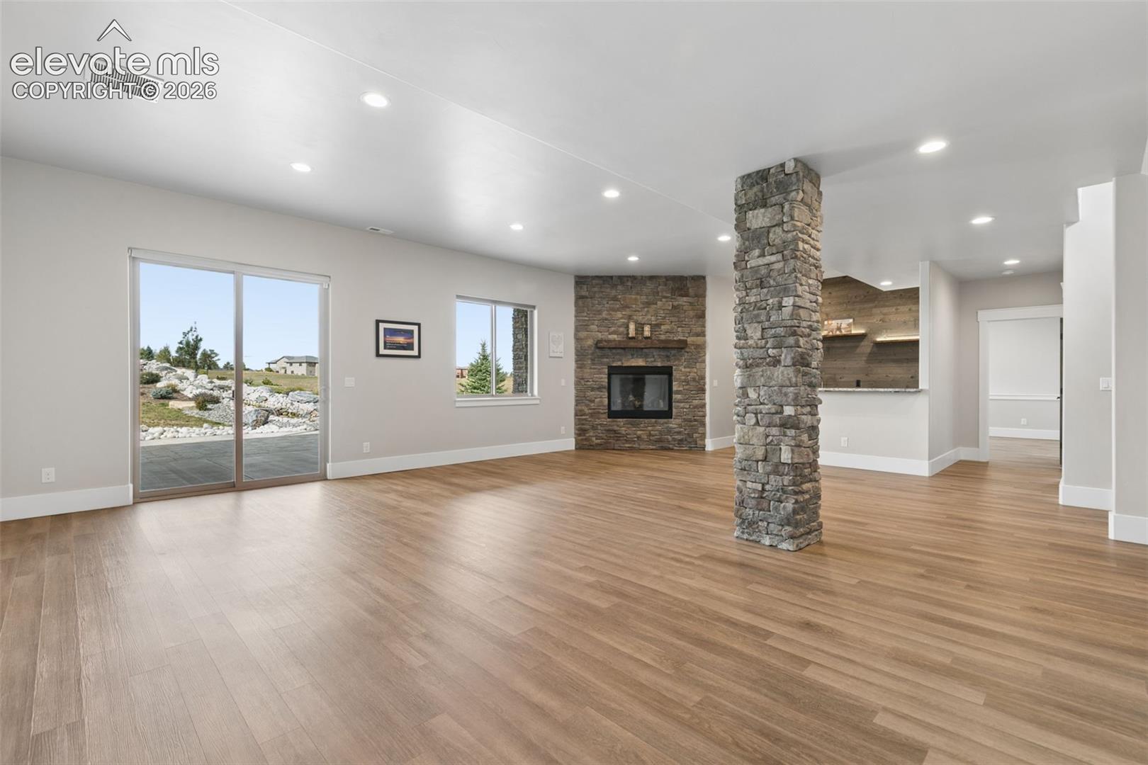 Spacious living area featuring wood-finish flooring, a stone-clad fireplace, built-in bar, and recessed lighting