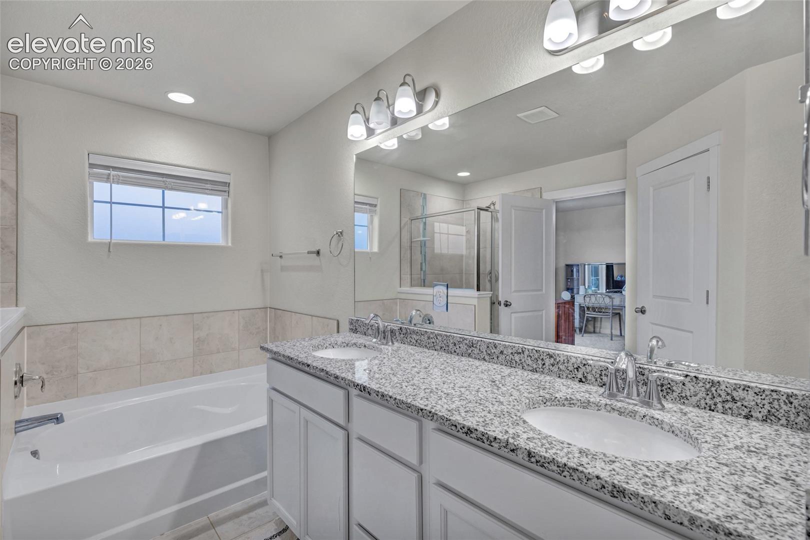 Double vanity with granite countertops and undermount sinks, flanked by a built-in bathtub with tiled surround and a glass-enclosed shower
