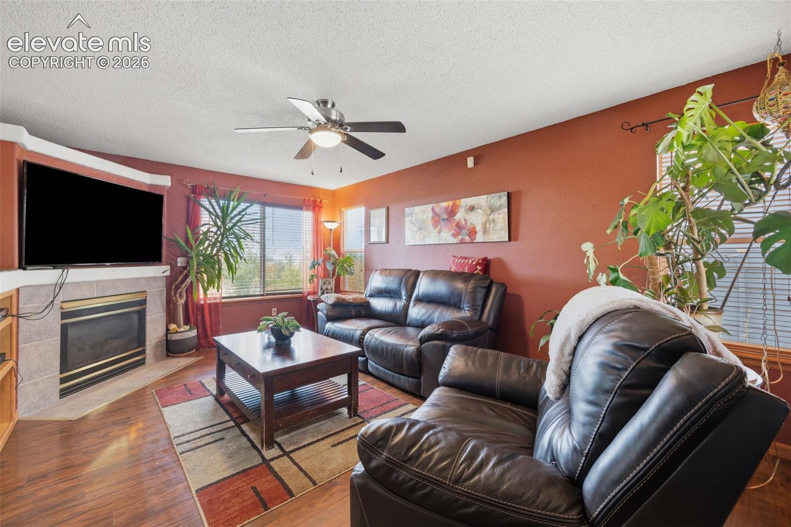 Living area featuring wood-finish flooring, a corner fireplace with a tiled surround, and large windows with privacy blinds