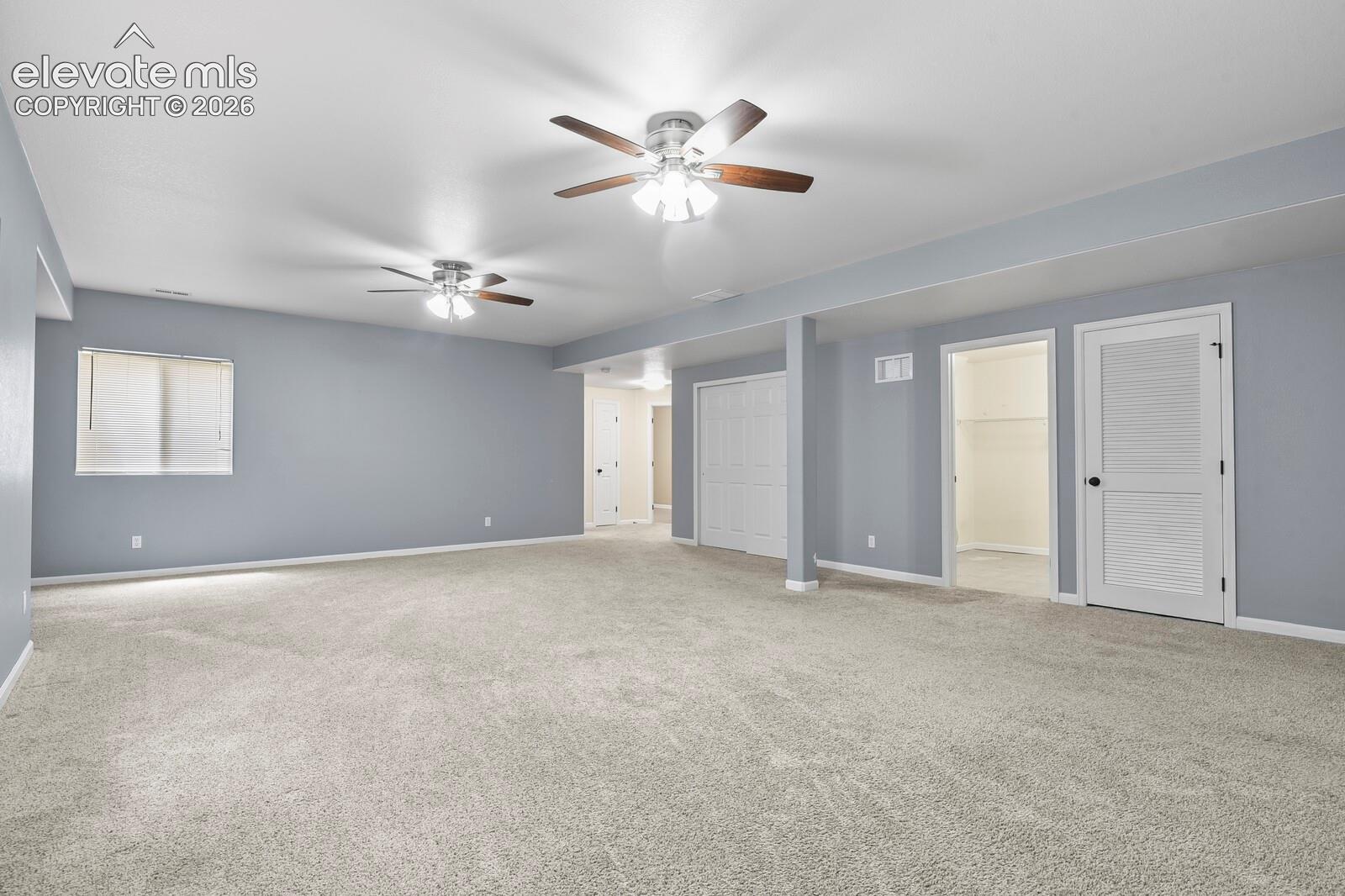 Spacious room featuring light beige carpeting, neutral wall paint, and two ceiling fans with integrated lighting