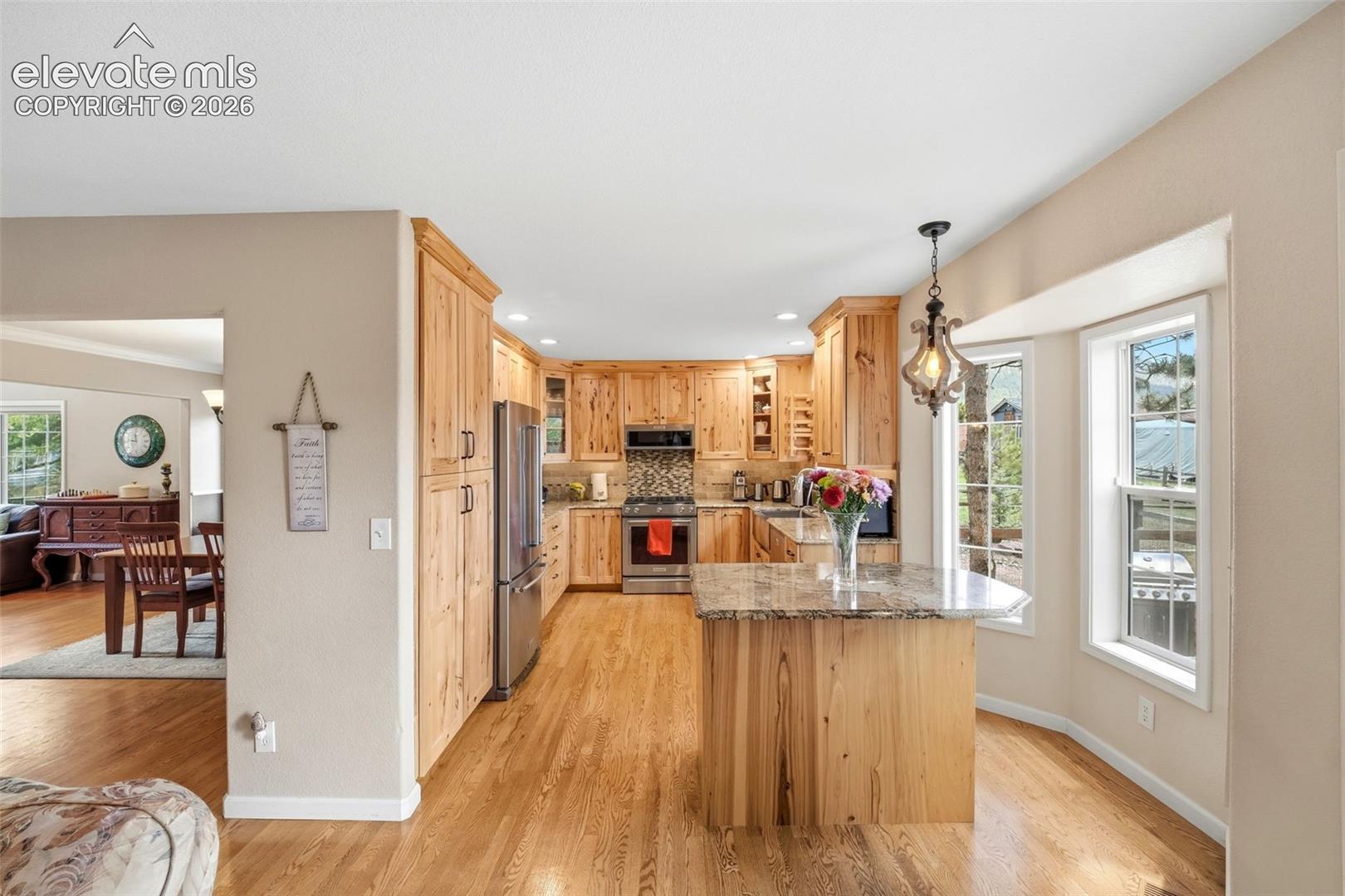 Kitchen featuring natural wood cabinetry, stainless steel appliances, a tile backsplash, and a granite-topped island with seating
