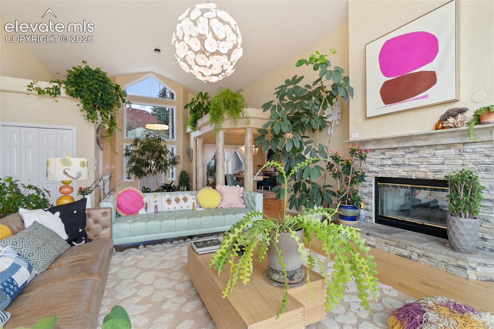 Living area featuring vaulted ceilings, a stacked stone fireplace, hardwood flooring, and a large arched window with transom above