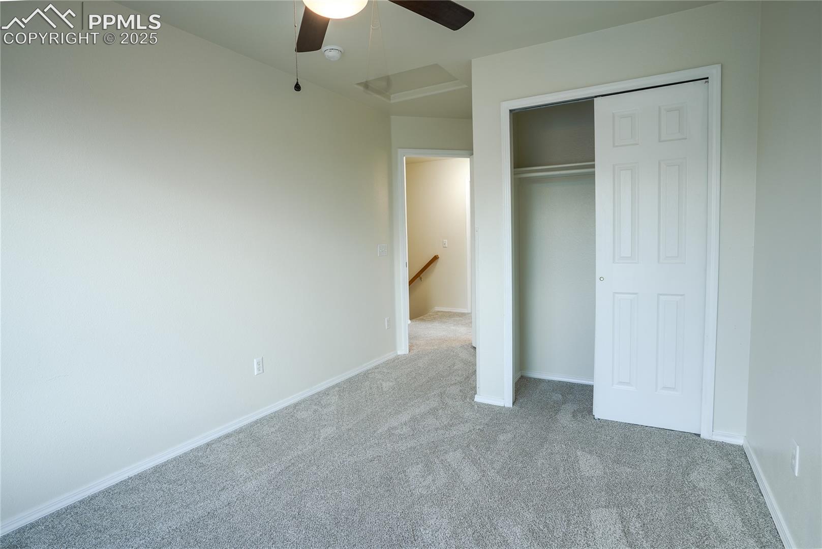 Unfurnished bedroom featuring carpet, a closet, a ceiling fan, and attic access