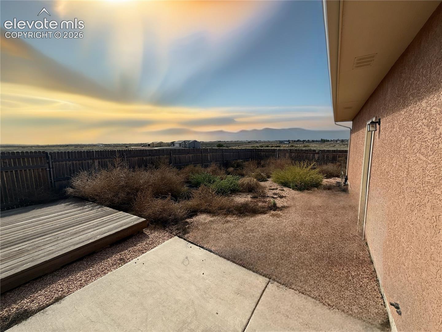 Backyard featuring a wood-finish deck, concrete patio, stucco exterior, and mountain backdrop