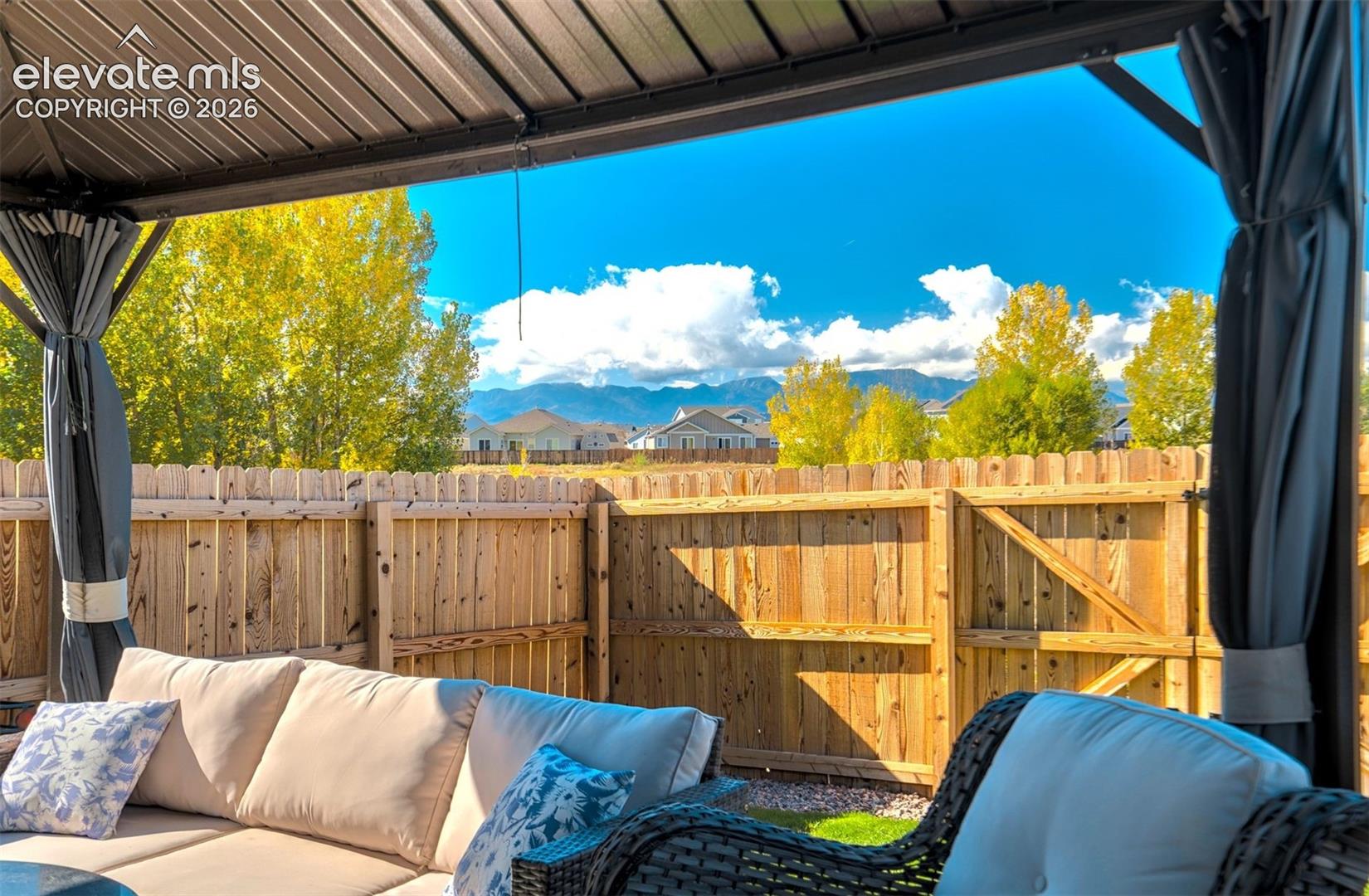 Outdoor space featuring a metal-framed gazebo, wooden privacy fencing, and mountain scenery