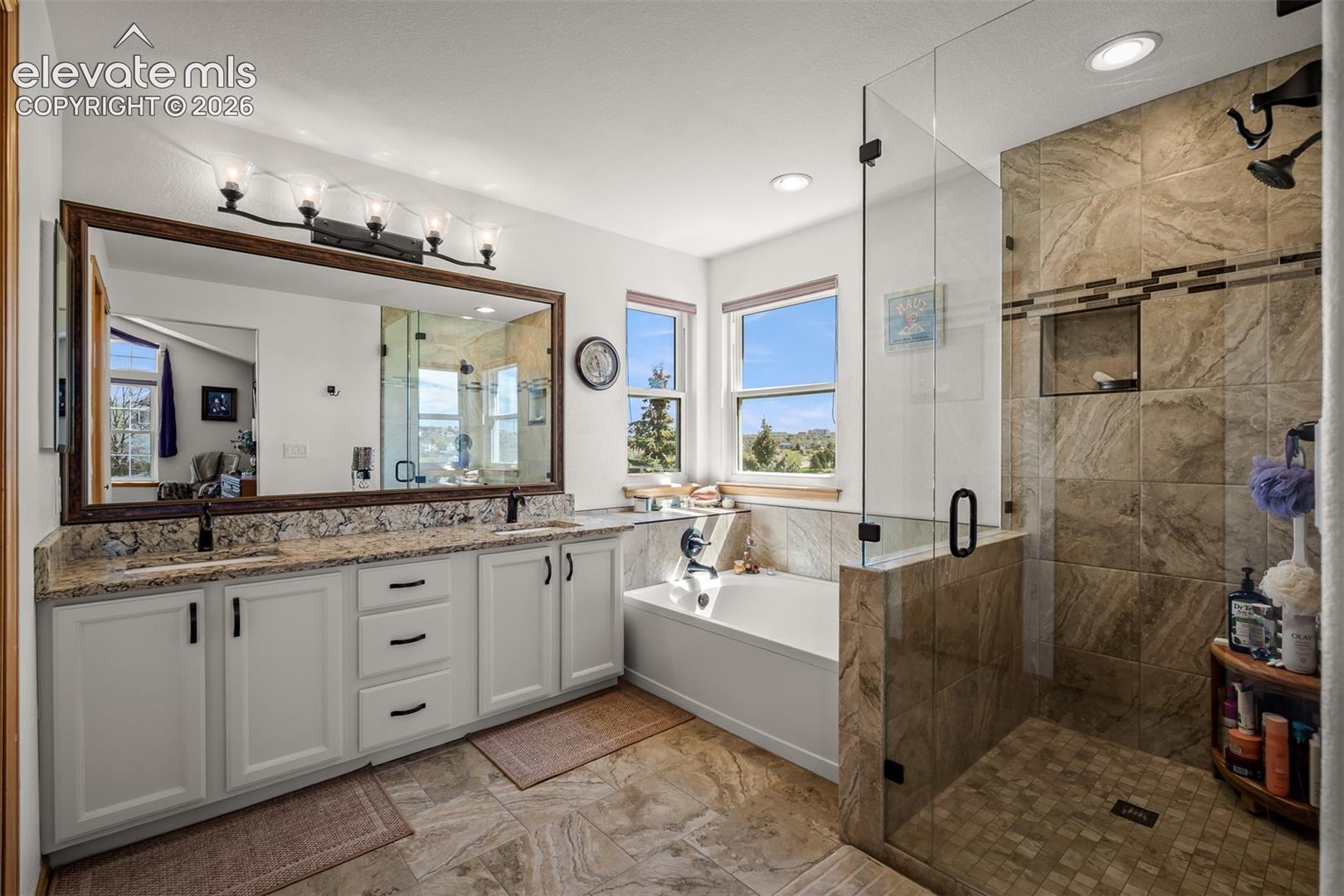 Spacious bathroom featuring a frameless glass shower enclosure with tile surround and integrated niche, a separate soaking tub, and a dual-sink vanity with quartz countertops.