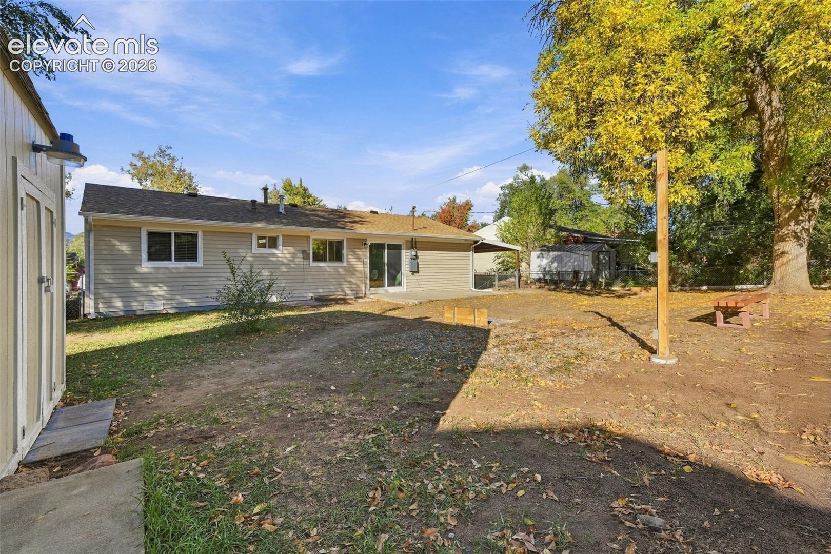 Rear exterior featuring light-colored horizontal siding, a concrete patio, a detached storage shed, and mature trees