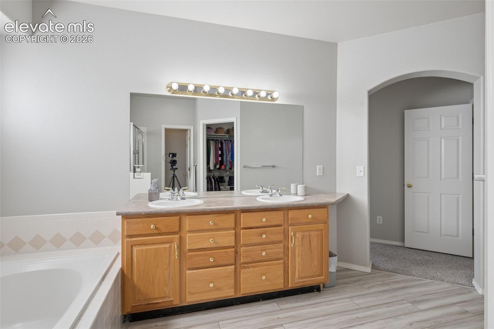 Double vanity with light-tone wood cabinetry, solid surface countertop, dual integrated sinks, and large wall-mounted mirror