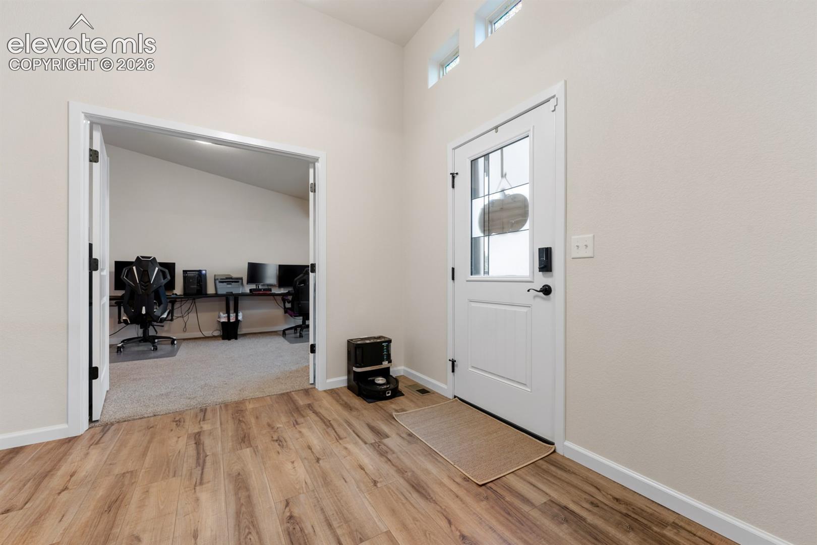 Entryway featuring wood-finish flooring, high ceilings, transom windows, and a glass-inset exterior door, with double doors opening to a carpeted room