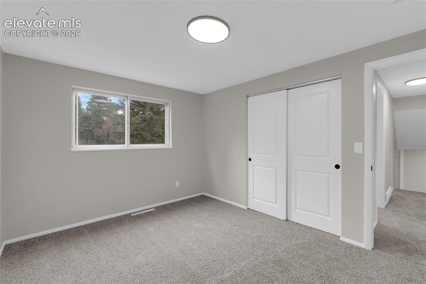 Neutral gray walls with white trim, gray carpeting, dual white sliding closet doors with black hardware, and a single window