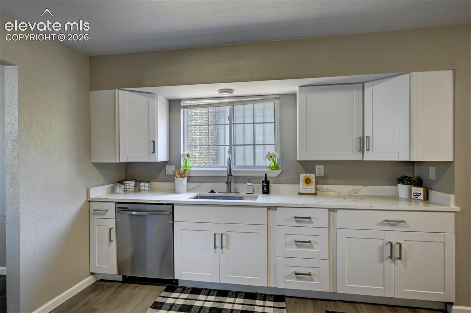 Kitchen featuring white shaker-style cabinetry, white countertops with grey veining, a stainless steel dishwasher, an undermount sink with a gooseneck faucet, and wood-finish flooring