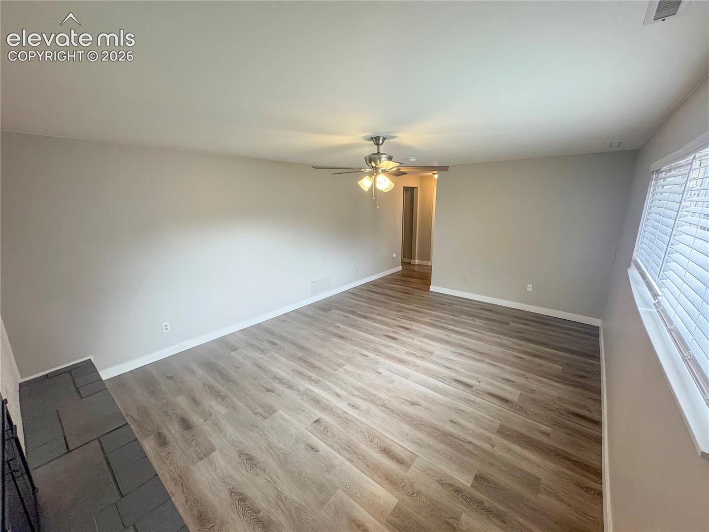 Wood-finish flooring, stone hearth, and central ceiling fan with integrated lighting