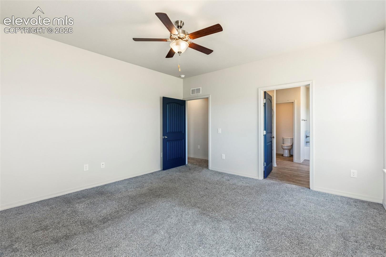 Spacious room featuring plush gray carpeting, crisp white walls, and a ceiling fan with integrated lighting