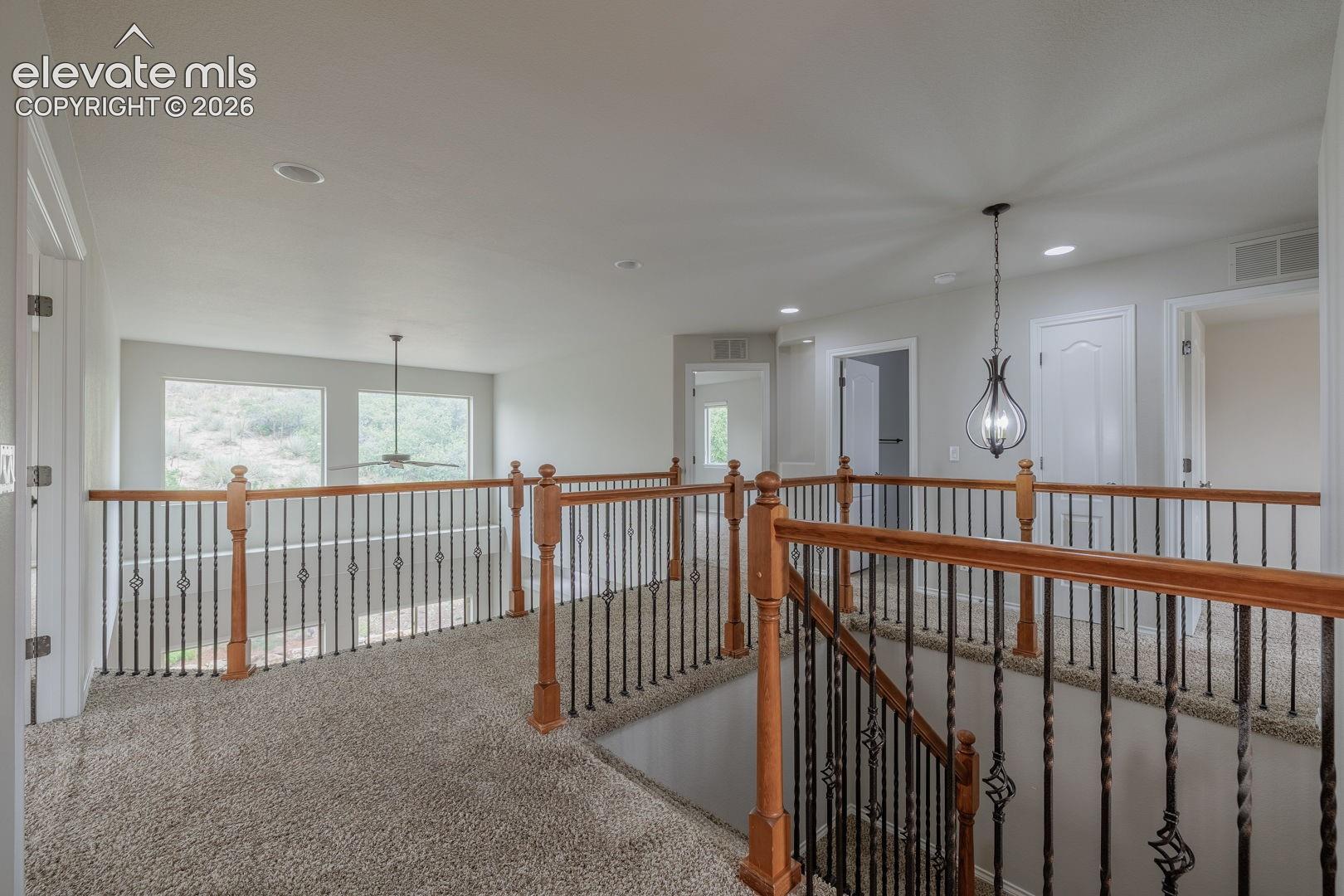 Carpeted upper landing to bedrooms featuring a wood and wrought iron staircase railing, recessed lighting, a ceiling fan, and multiple interior doorways