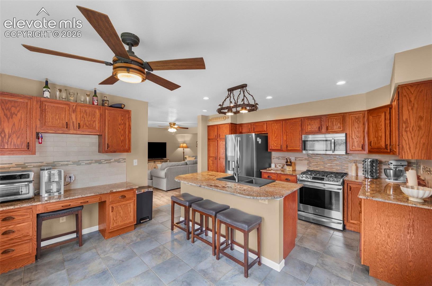 Kitchen featuring wood cabinetry, light-toned countertops, a central island with bar seating, stainless steel appliances, and tile flooring