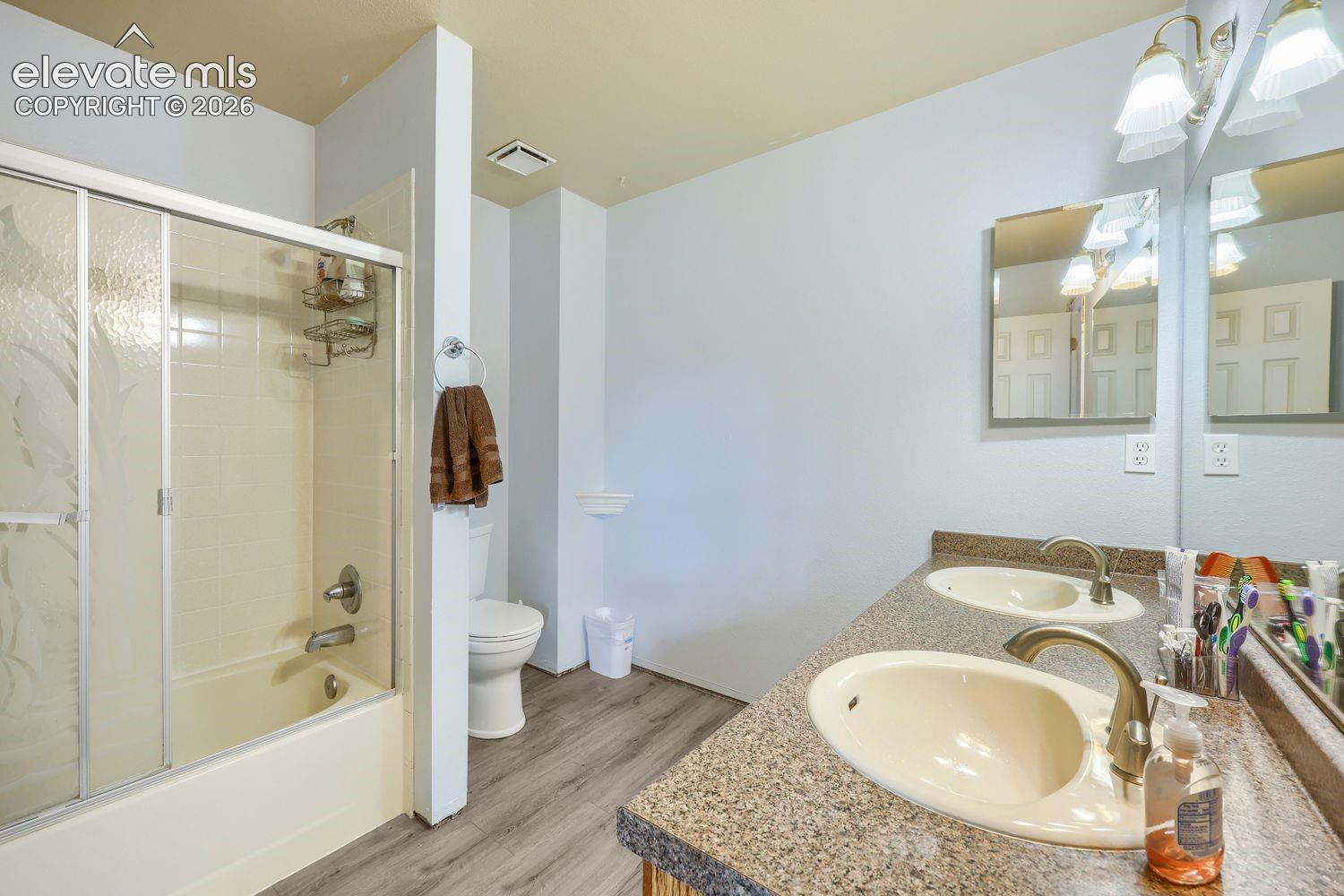 Dual vanity with integrated sinks, brushed nickel fixtures, wood-finish flooring, and a tub/shower combination with sliding glass doors