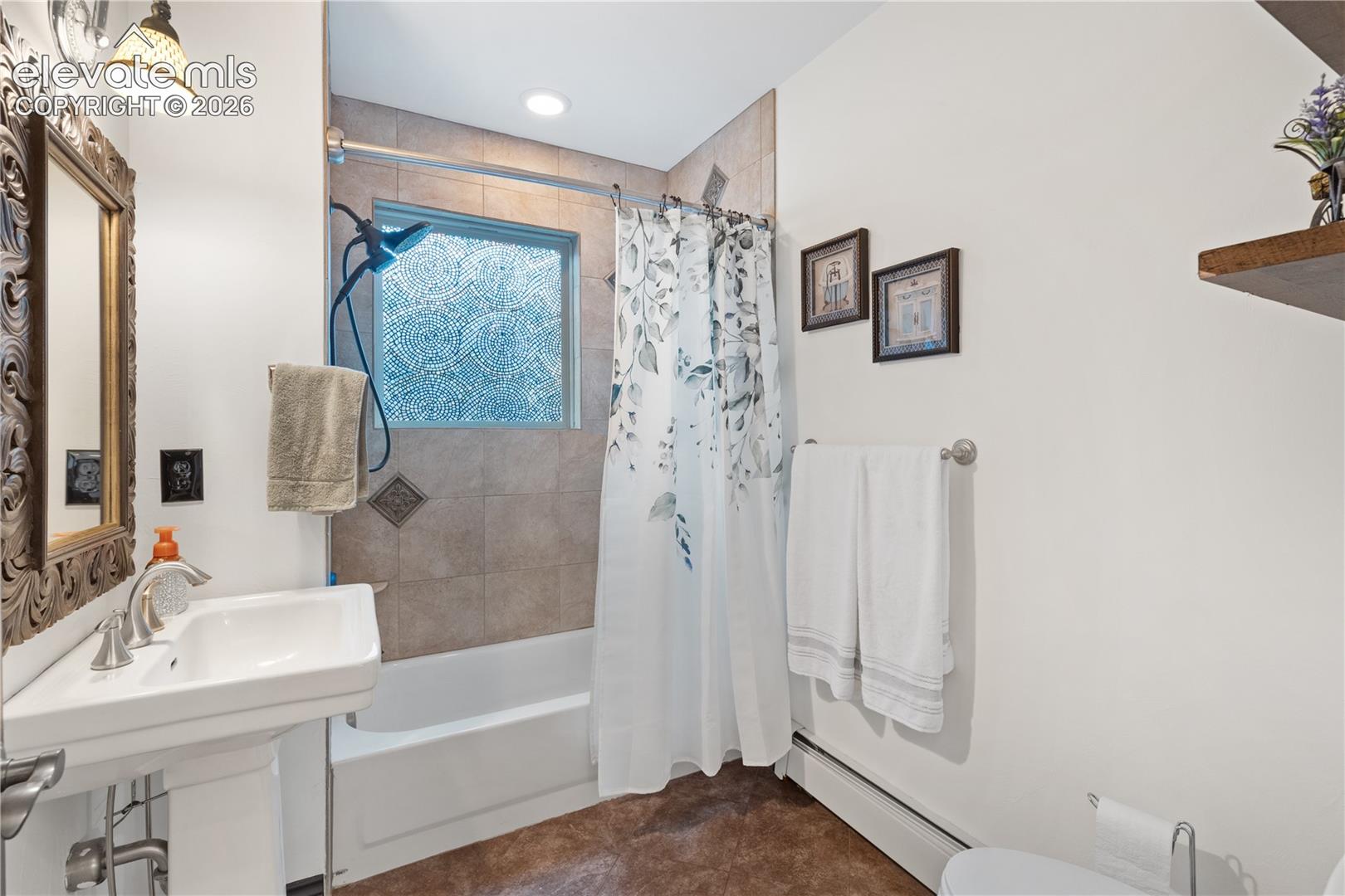 Bathroom featuring a pedestal sink, tub with a shower fixture, and a tiled shower surround with a frosted window