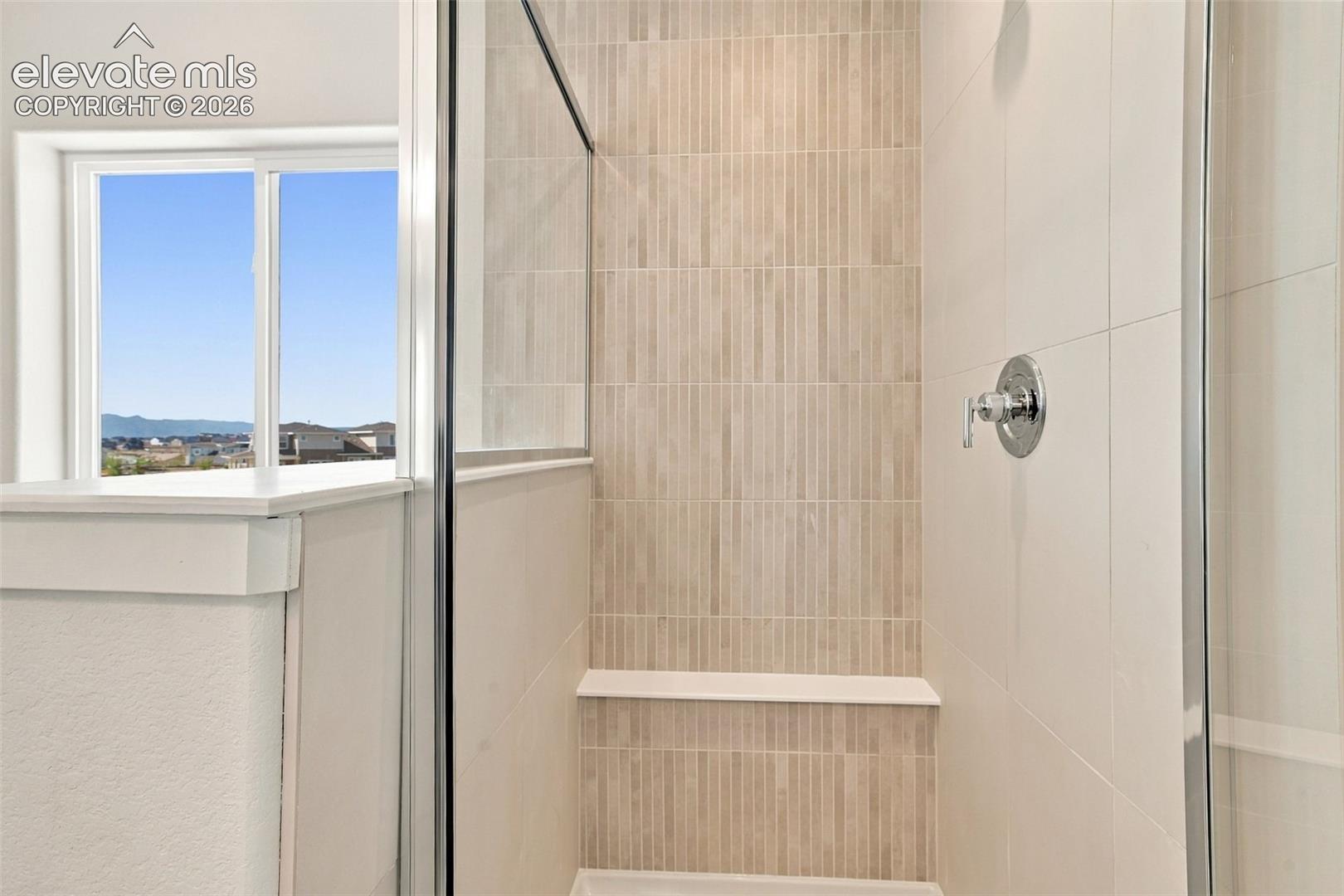 Walk-in shower with clear glass enclosure, tiled walls, built-in bench, and polished chrome fixtures