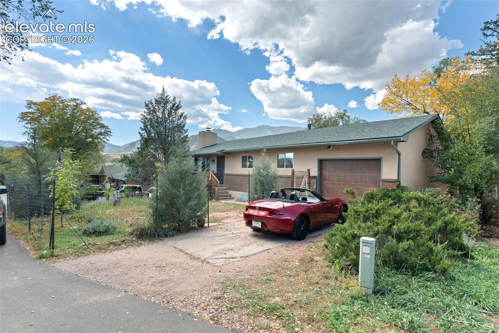 Single-level residence with an attached garage, paved driveway, mature landscaping, and a mountain backdrop