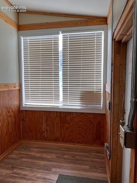 Wood-paneled interior walls, window with horizontal blinds, wood-finish flooring, and exposed trim work