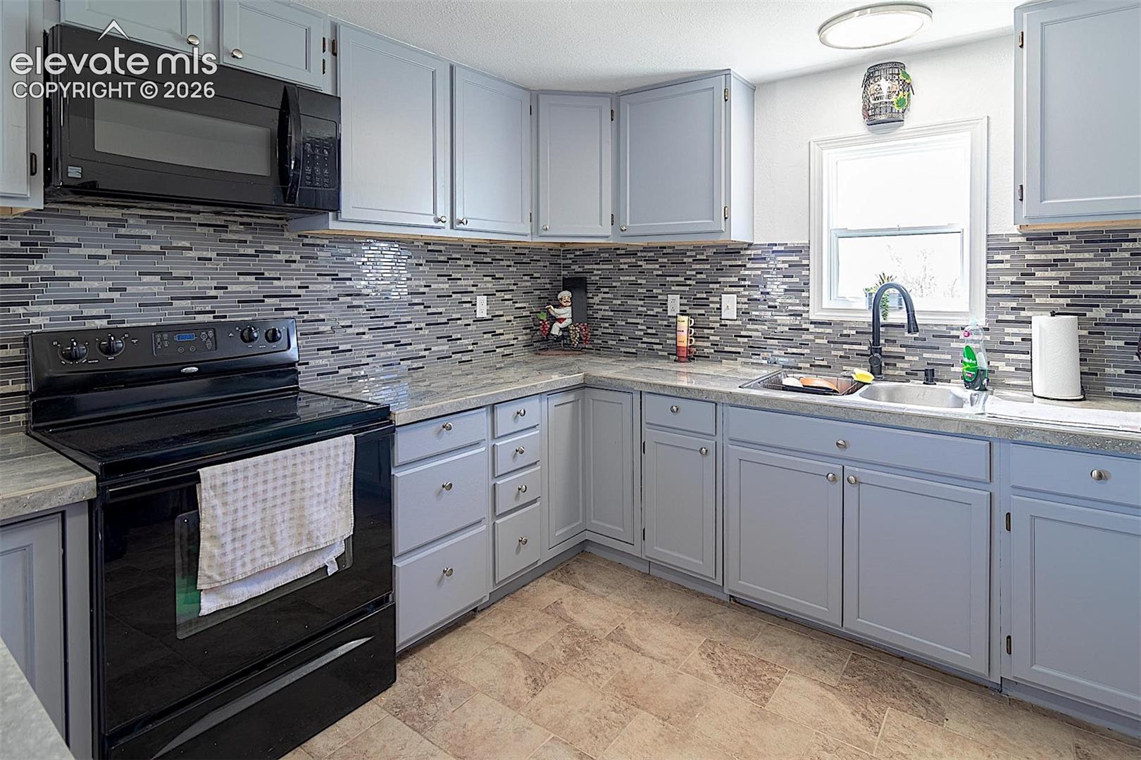 Kitchen with black appliances, a sink, decorative backsplash, and light countertops