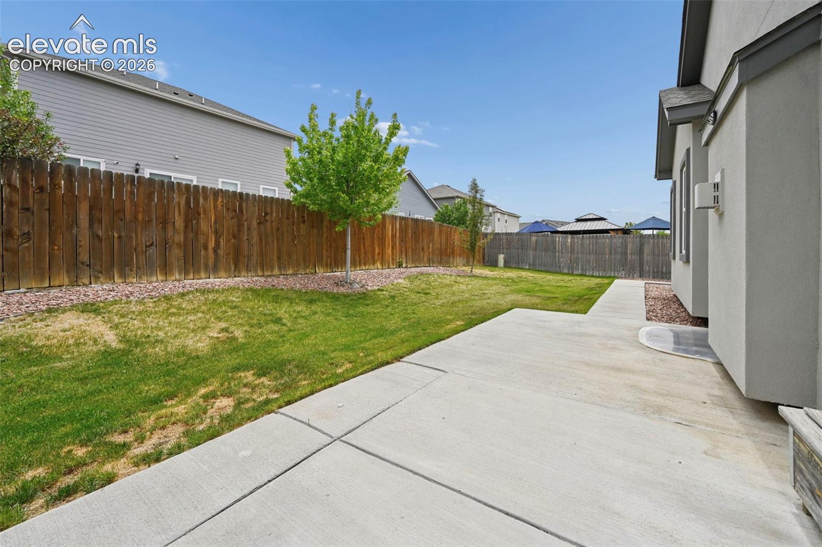 Rear exterior featuring a concrete patio, grass lawn, and full-height wood privacy fencing