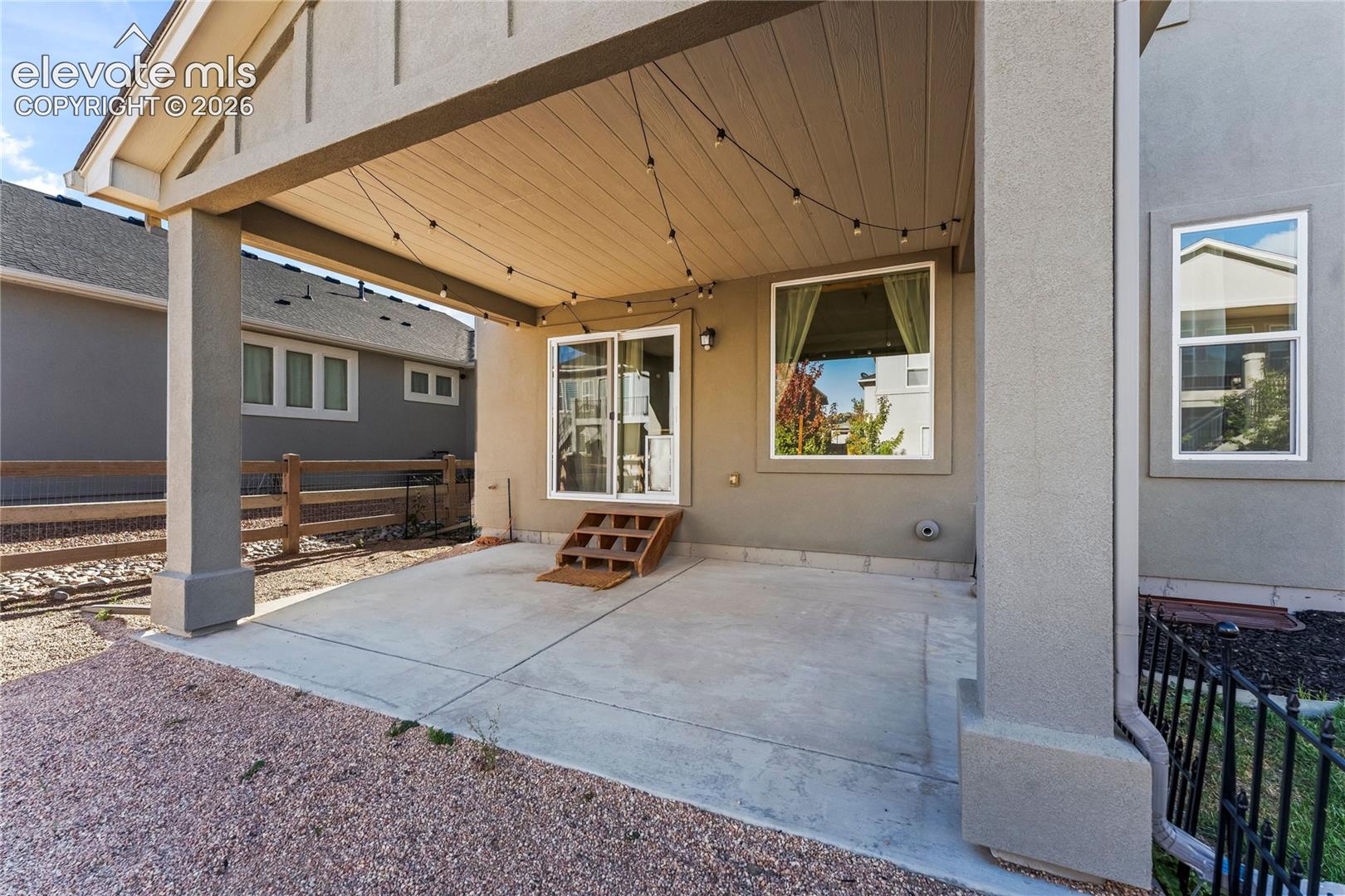 Covered patio with a concrete floor, high ceiling with exposed beam detail, sliding glass door entry, and stone-finish exterior siding