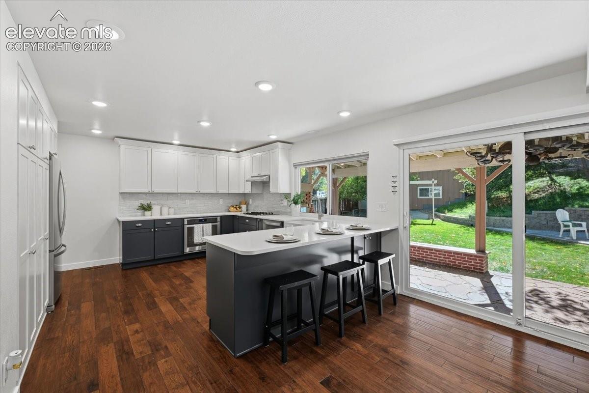Kitchen featuring wood flooring, two tone cabinetry, recessed lighting, a peninsula with countertop seating, and sliding glass doors to outdoor hardscaping