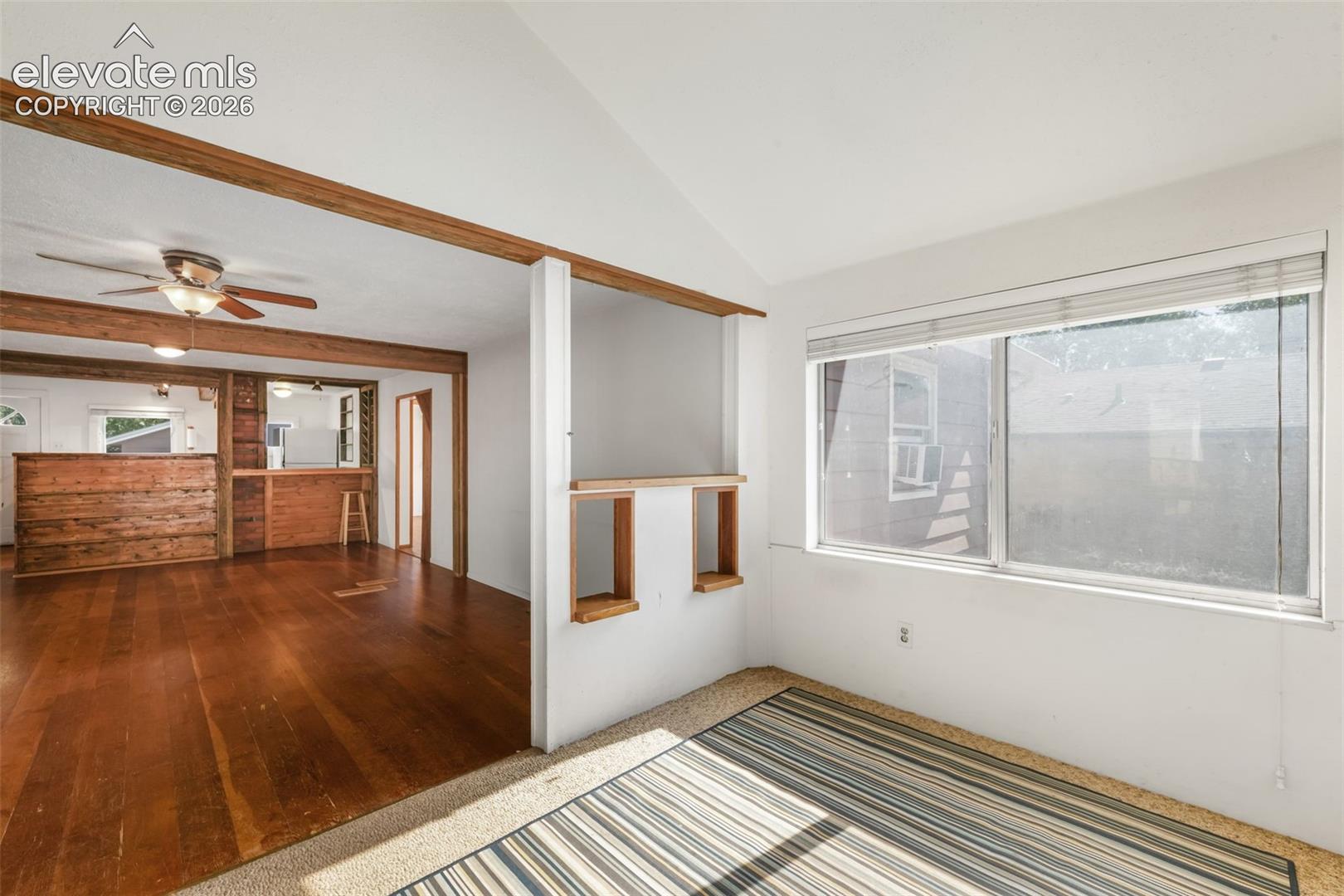 Vaulted ceiling, wood-finish flooring, wood beam accents, built-in pass-through, and ceiling fan with light fixture