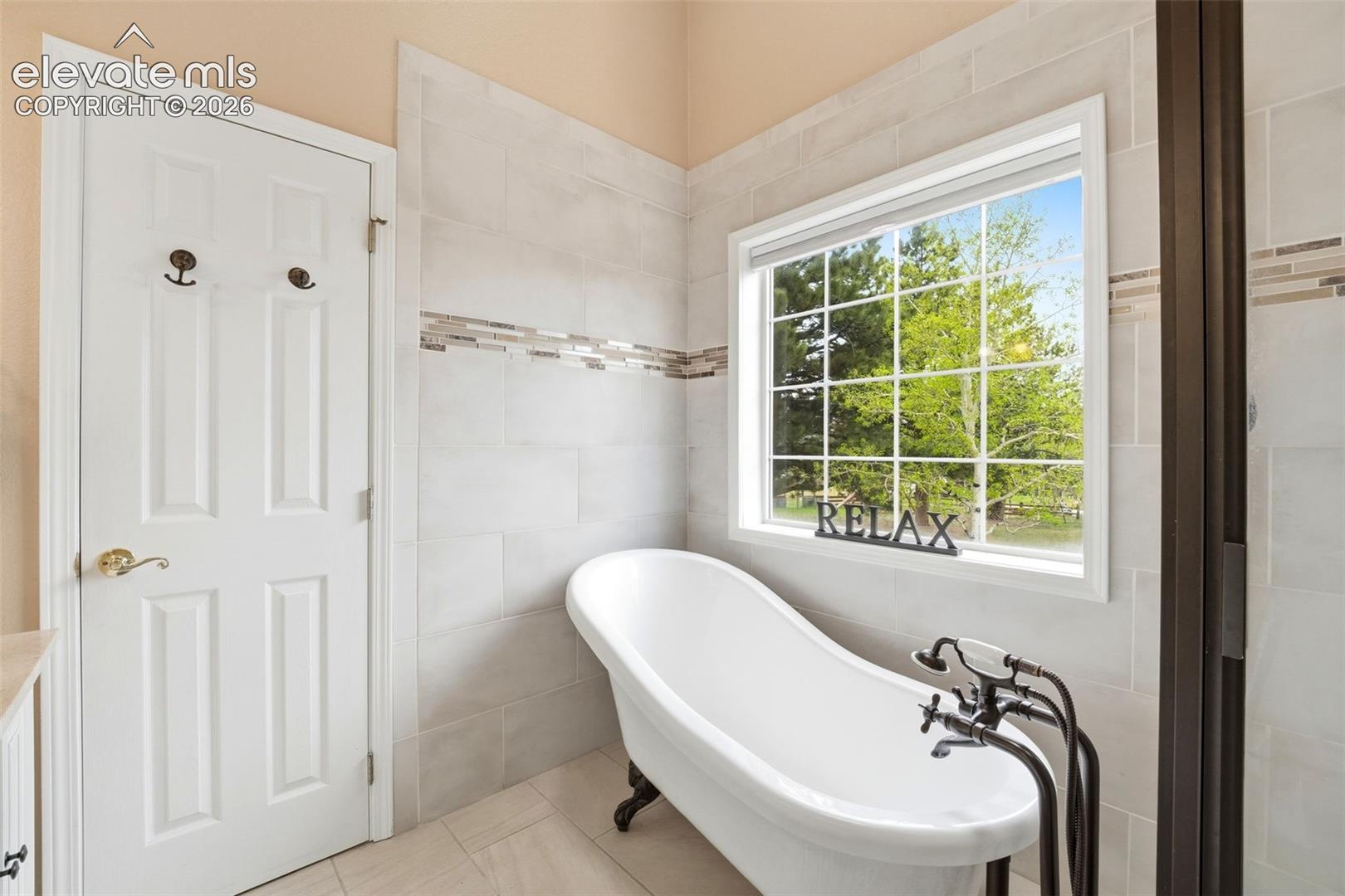 Freestanding clawfoot tub with floor-mounted fixtures, set against a tiled wall with decorative accent banding
